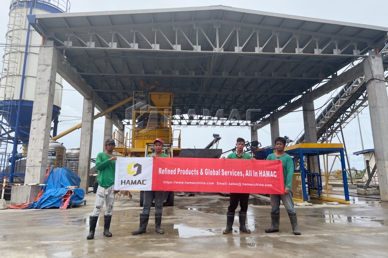On-site personnel holding a HAMAC banner beside concrete block production equipment in the Philippines